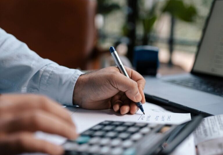 Free A person calculating finances with a calculator and pen on a desk indoors. Stock Photo